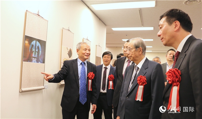 “湖州印象”攝影展主創(chuàng)、世界華人攝影協(xié)會副會長馮學敏向吳江浩大使、福田康夫前首相等嘉賓介紹展出作品。（人民網(wǎng) 許可攝）