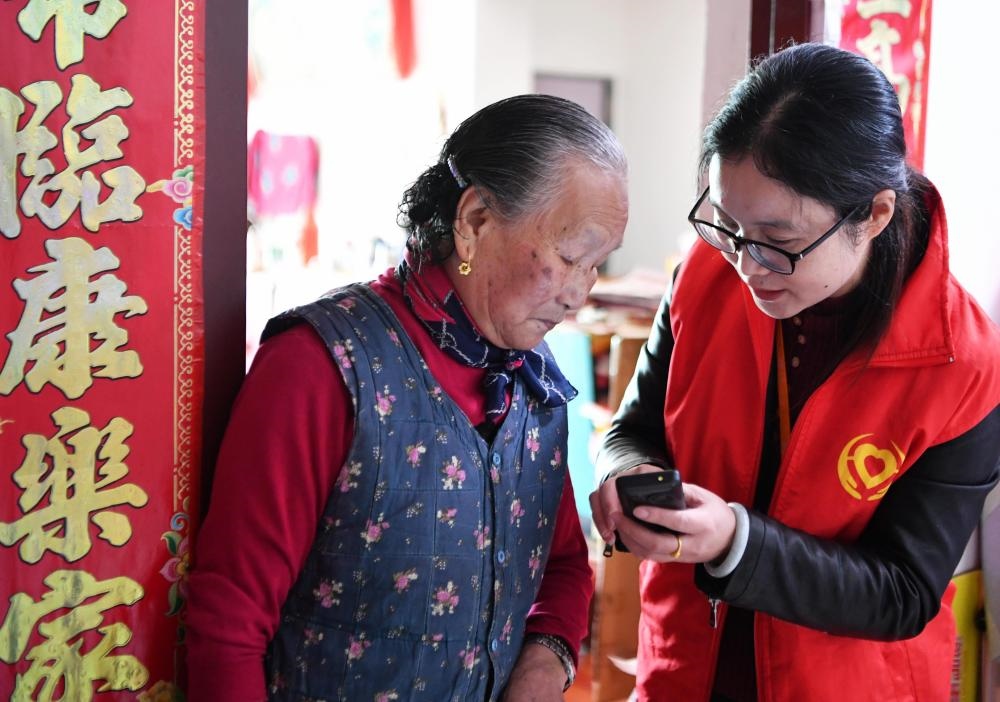 在福州市長樂區(qū)航城街道籌岐村，智慧養(yǎng)老平臺派駐社區(qū)的助老員（右）在為老人陳鳳英（左）講解養(yǎng)老定制手機(jī)的用法（2021年11月26日攝）。新華社記者 魏培全 攝