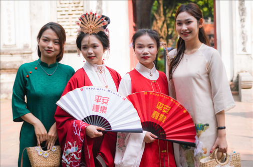 身穿古裝的中國游客和身穿越南傳統(tǒng)服飾奧黛的越南青年在文廟門前合影。