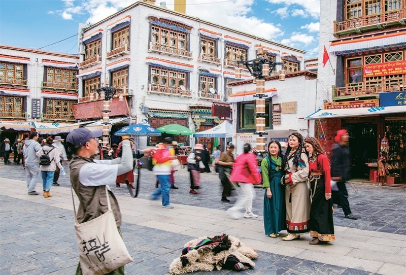 千年八廓街，見證民族團(tuán)結(jié)。2021年7月，習(xí)近平總書記來到位于西藏拉薩老城區(qū)的八廓街，感慨地說：“千年八廓街，是我們各民族建起來的八廓街。各民族文化在這里交流交往交融，我們中華民族的大家庭在這里其樂融融?！眻D為2023年6月13日，游客身著藏裝在八廓街拍照留念。 新華社記者 姜帆/攝