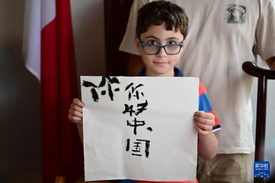 7月4日，在馬耳他桑塔露琪亞市的中國(guó)古典園林“靜園”，一名男孩展示他的書(shū)法作品。新華社發(fā)（喬納森·博格 攝）