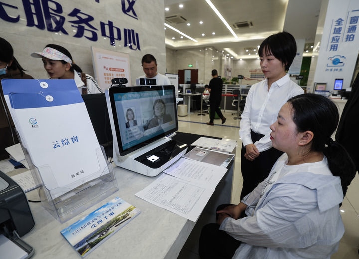 在浙江省嘉興市秀洲區(qū)王江涇鎮(zhèn)便民服務(wù)中心的“跨域通辦·云綜窗”窗口，辦理開業(yè)登記的個體工商戶（右一）通過該系統(tǒng)與江蘇省蘇州市吳江區(qū)盛澤鎮(zhèn)行政審批局工作人員視頻連線，進(jìn)行身份讀取及材料線上審核（2024年5月9日攝）。新華社記者 徐昱 攝