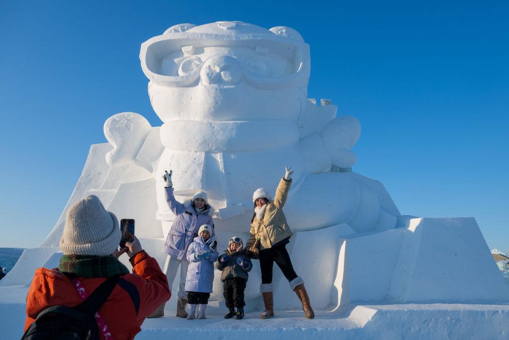2025年1月3日，在黑龍江哈爾濱冰雪大世界園區(qū)，游客與亞冬會(huì)吉祥物雪雕“濱濱”合影